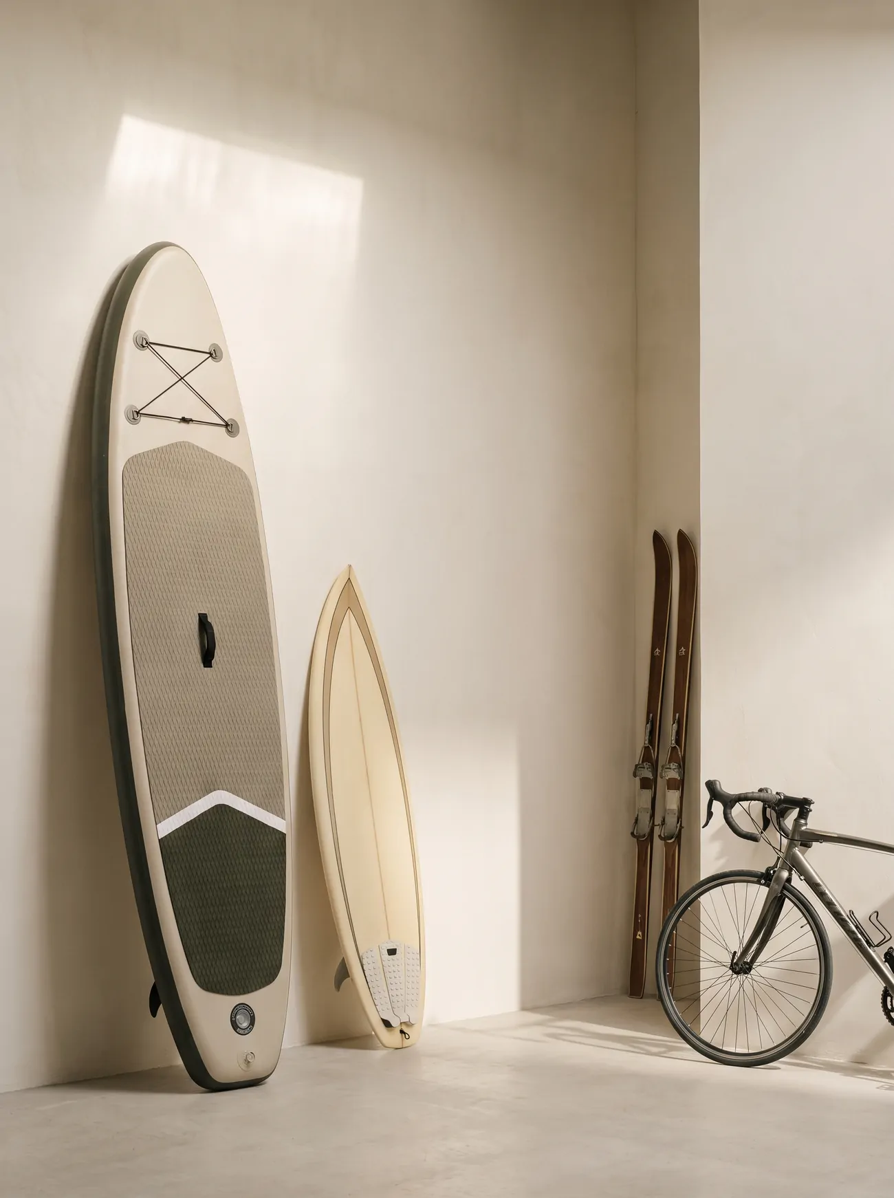 A paddleboard, surfboard, skis and a road bike stored against a wall