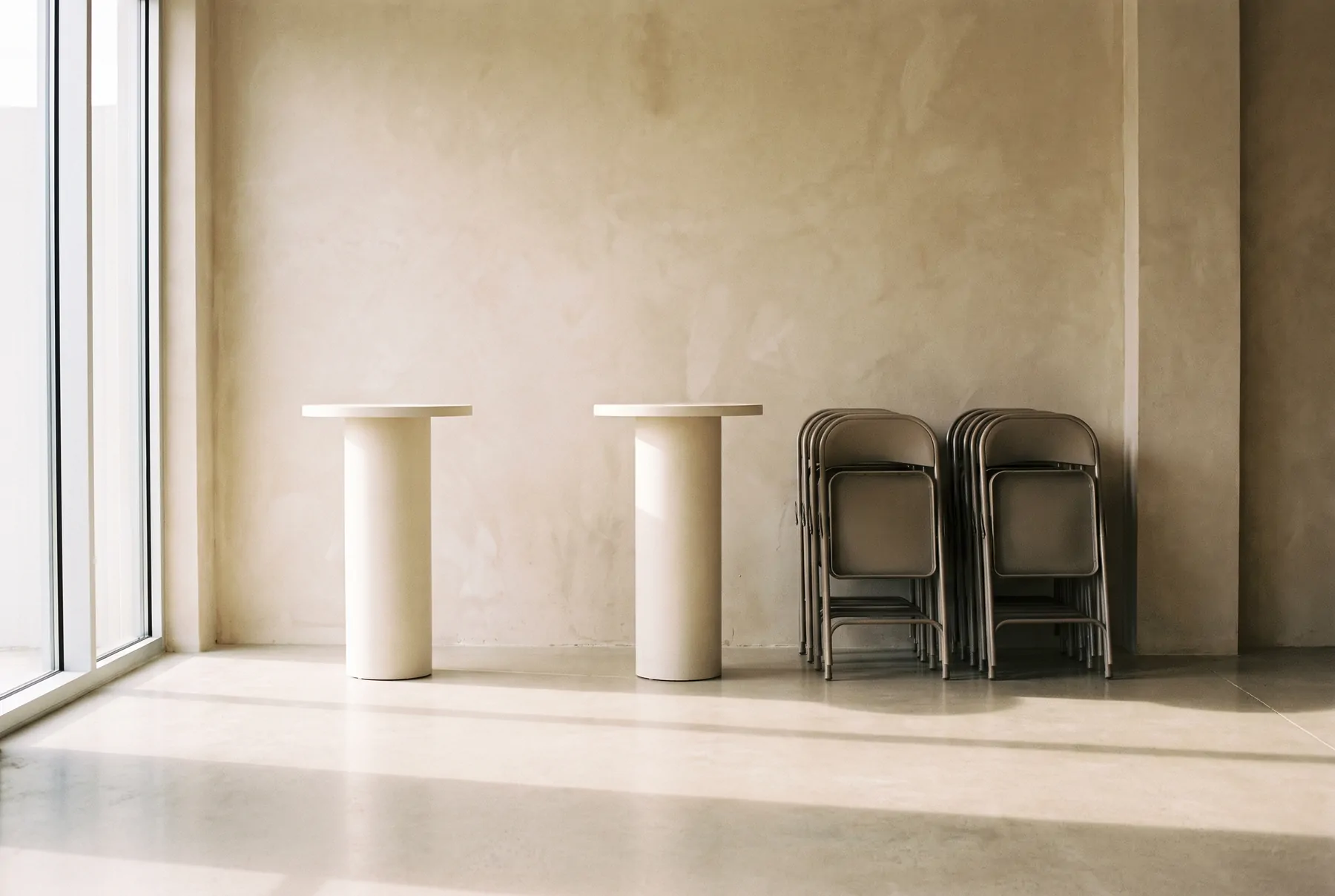 Two standing tables and a stack of folded chairs against a wall