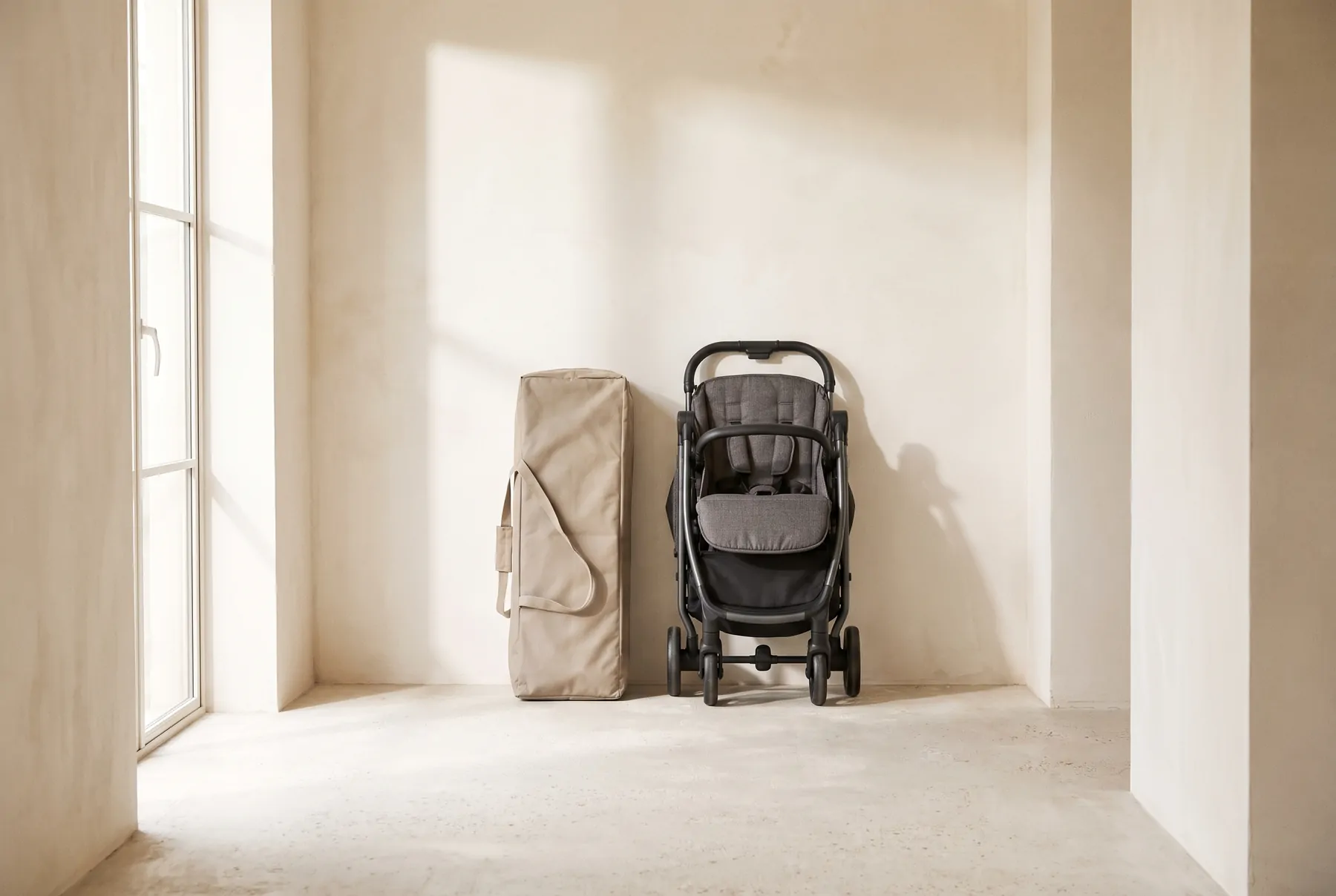 A folded travel cot in its bag beside an upright folded pushchair